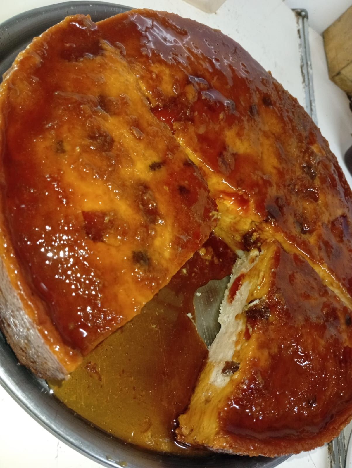  pastel redondo de color marrón dorado cubierto con un glaseado brillante de color ámbar oscuro en un molde de metal.