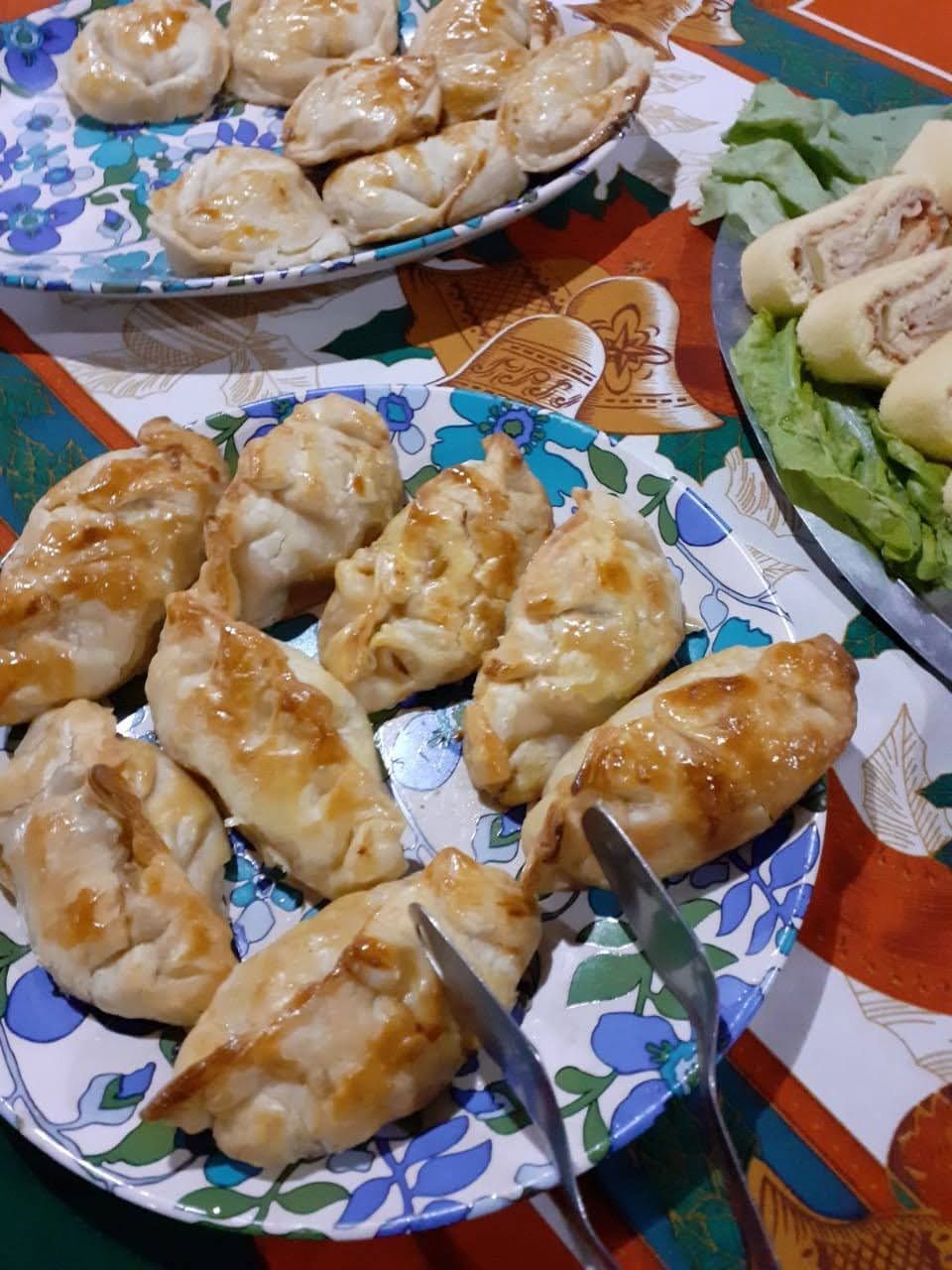 Empanadas doradas al horno dispuestas en platos florales junto a una bandeja de panecillos