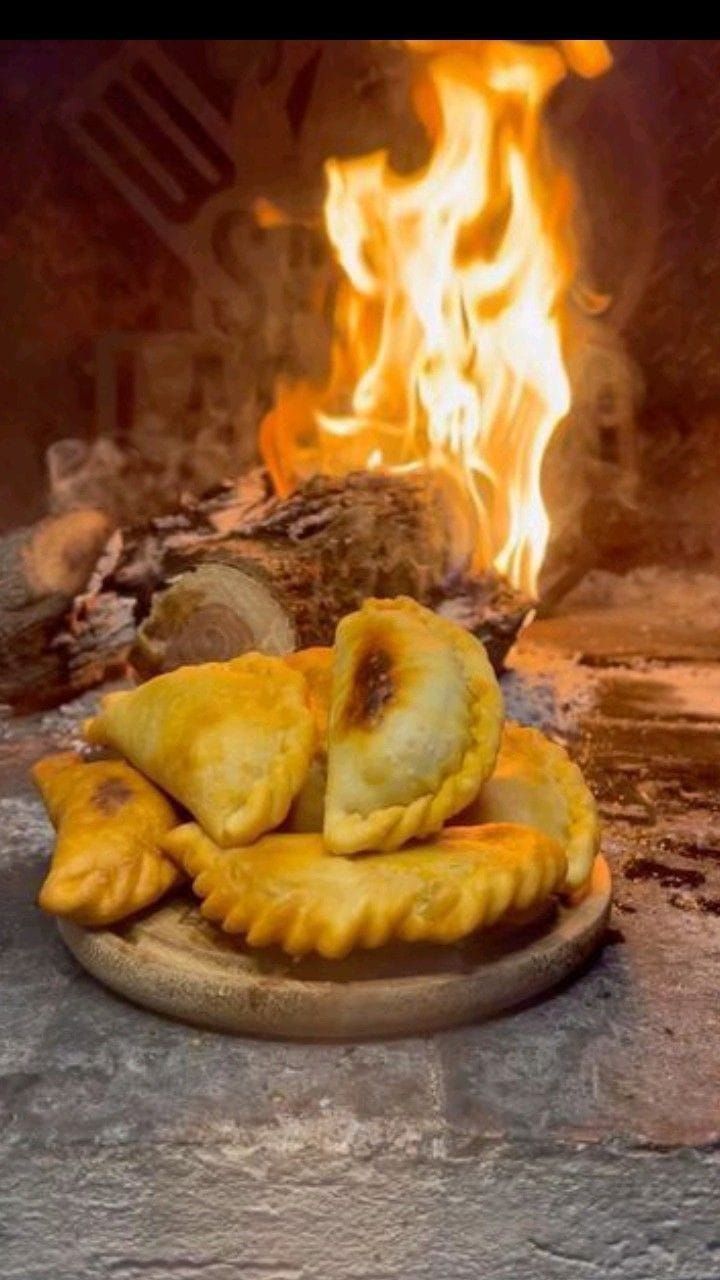 Un plato de empanadas doradas reposa frente a un fuego cálido y crepitante.