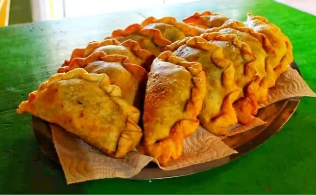 Un plato de empanadas fritas, doradas y dobladas, dispuestas sobre una servilleta de papel sobre una mesa verde.