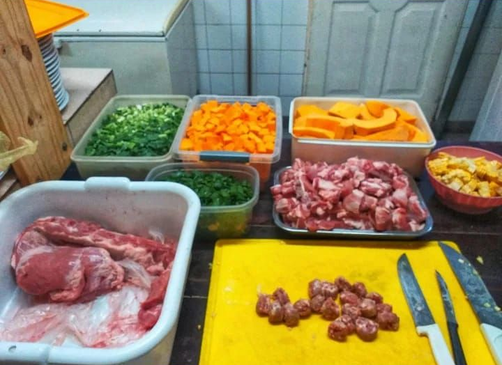 Una encimera de cocina comercial con cuencos y recipientes de verduras picadas, carne cruda y embutidos