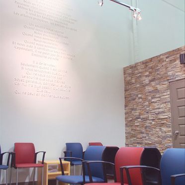 Salle d'attente avec des chaises rouges et bleues contre un mur blanc avec du texte et un mur d'accent en pierre.