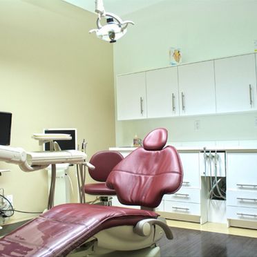 Un cabinet dentaire avec un fauteuil, du matériel et des armoires rouges. La pièce est décorée de murs vert clair et d'un éclairage dentaire au plafond.