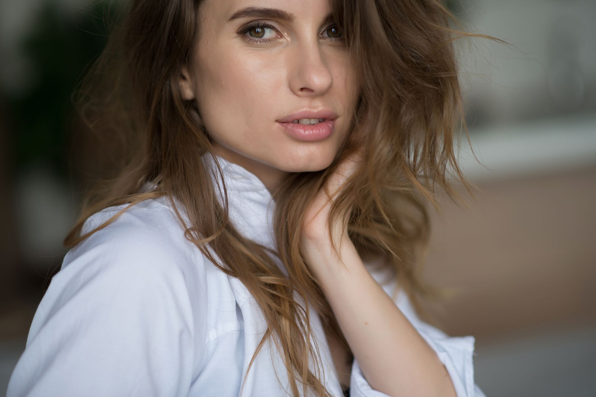 Woman with wavy brown hair, wearing a white shirt, gazing at the camera with a soft expression.