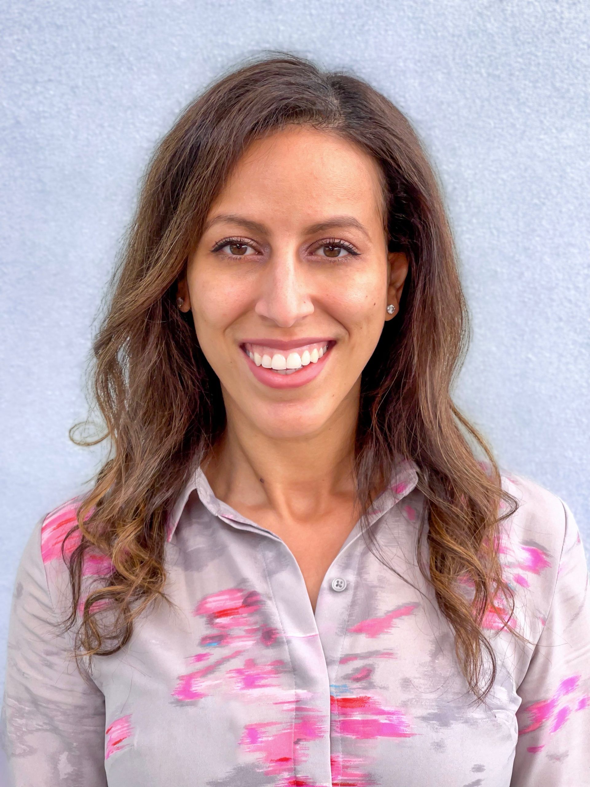 a portrait of Dr. Jackie Beshir, Board-Certified Dermatologist wearing a pink button down blouse