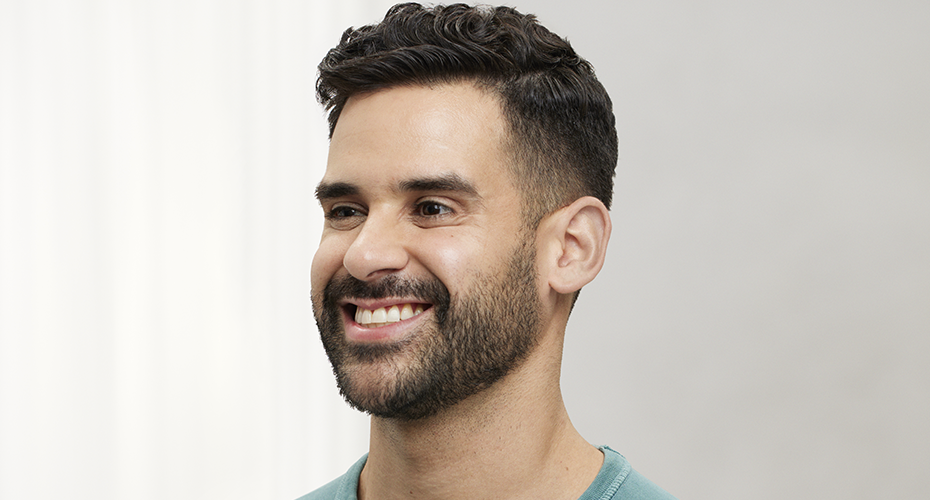 a man with a full beard, facing left is smiling, wearing a blue shirt after Botox treatment