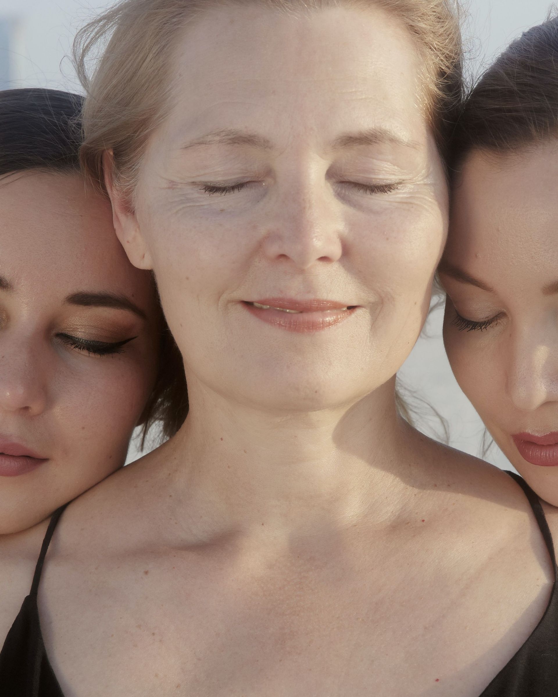 close up photo of two women leaning on another woman's shoulders smiling