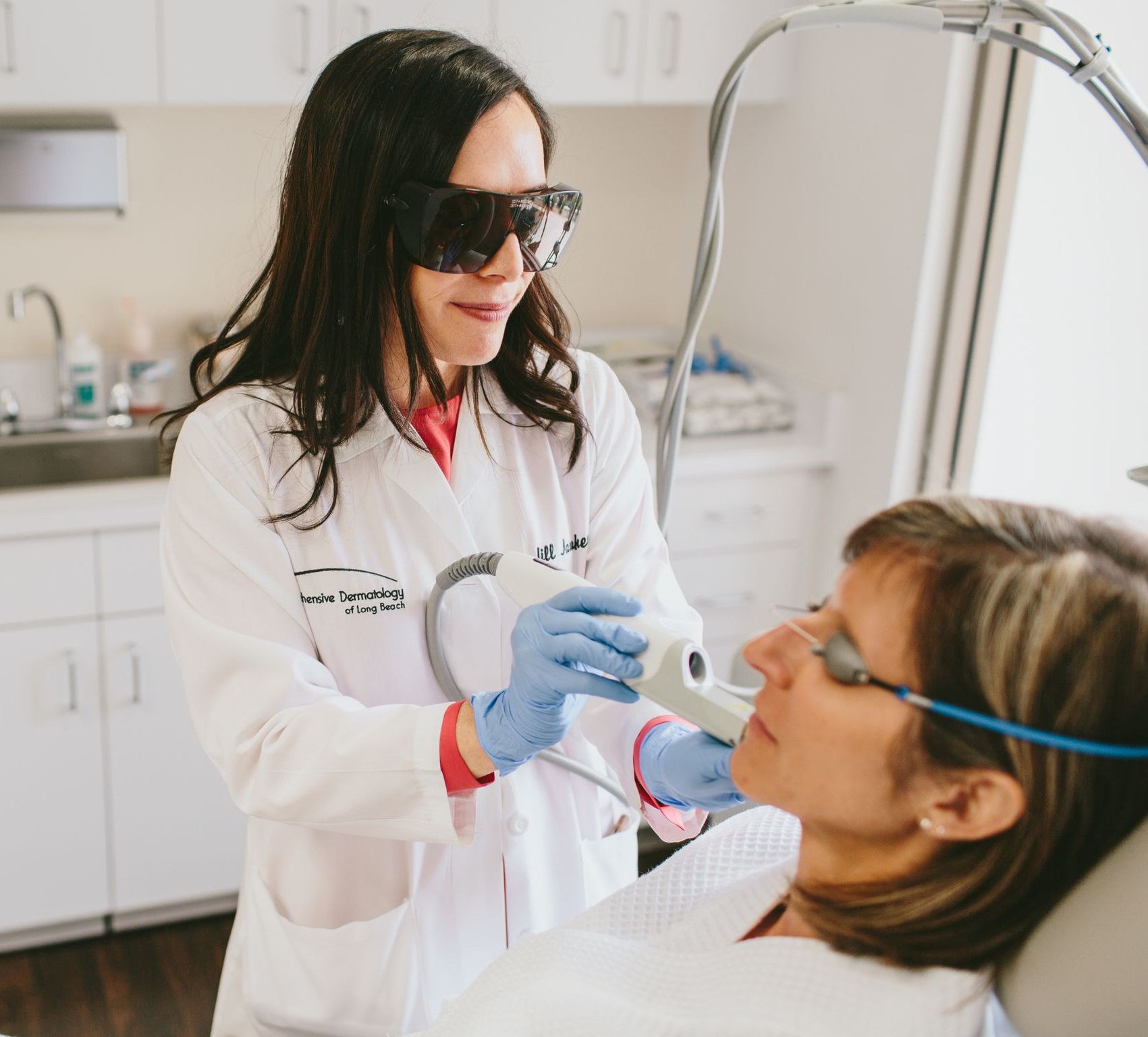 Dr. Jill Jahavery is wearing protective glasses as she applies laser treatment to a woman's face