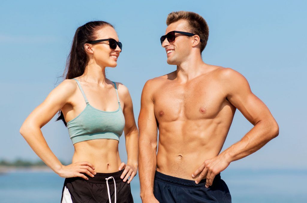 a toned man and a woman are standing next to each other on the beach wearing workout clothes