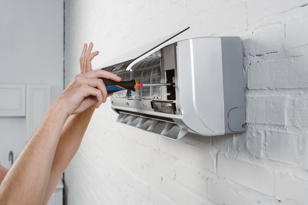 A Person Repairing A Wall-mounted Air Conditioner With A Screwdriver — Stanayr Electrical in Gulliver, QLD