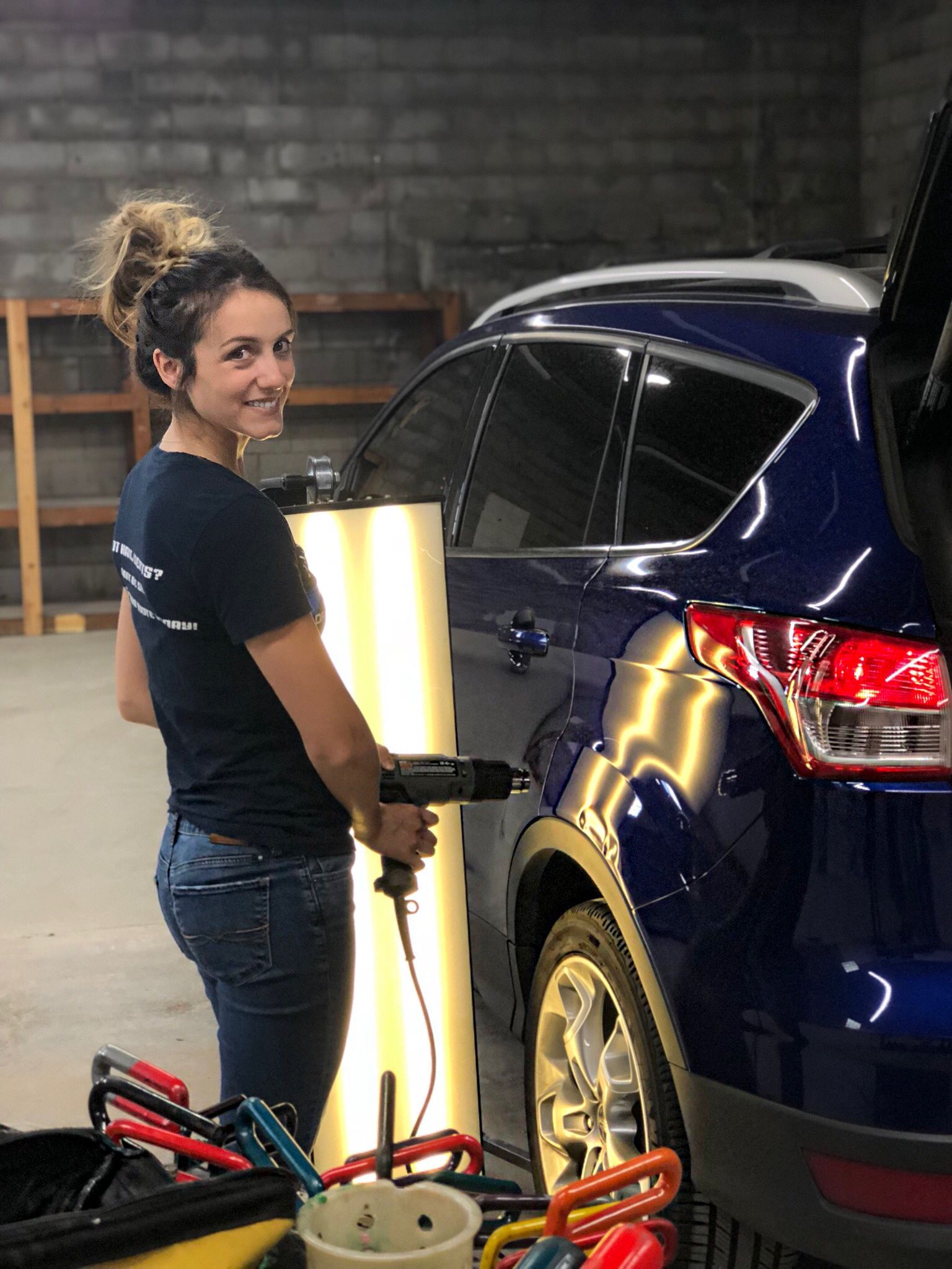 A woman is working on a blue car in a garage.