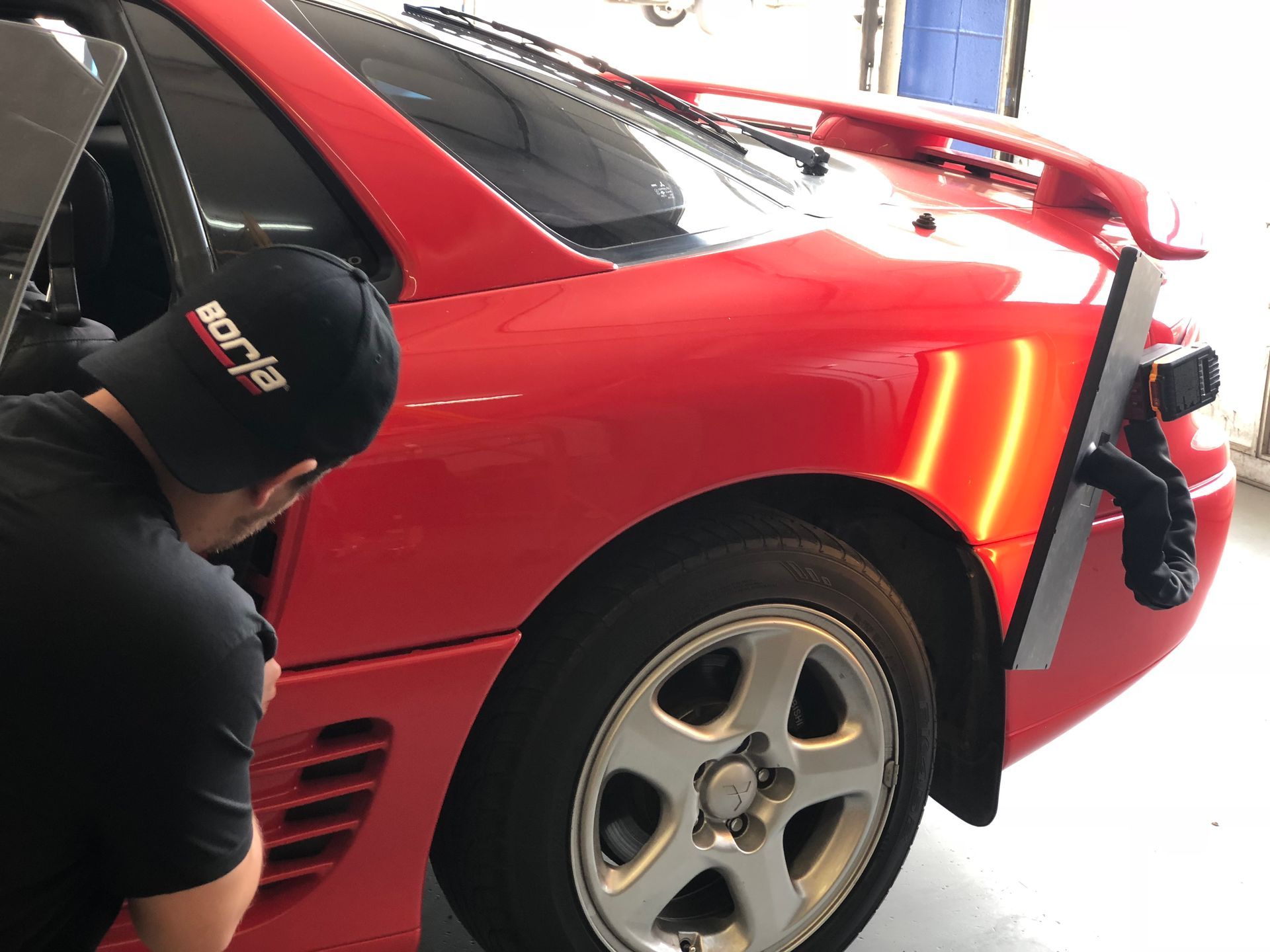 A man wearing a racing hat is working on a red car