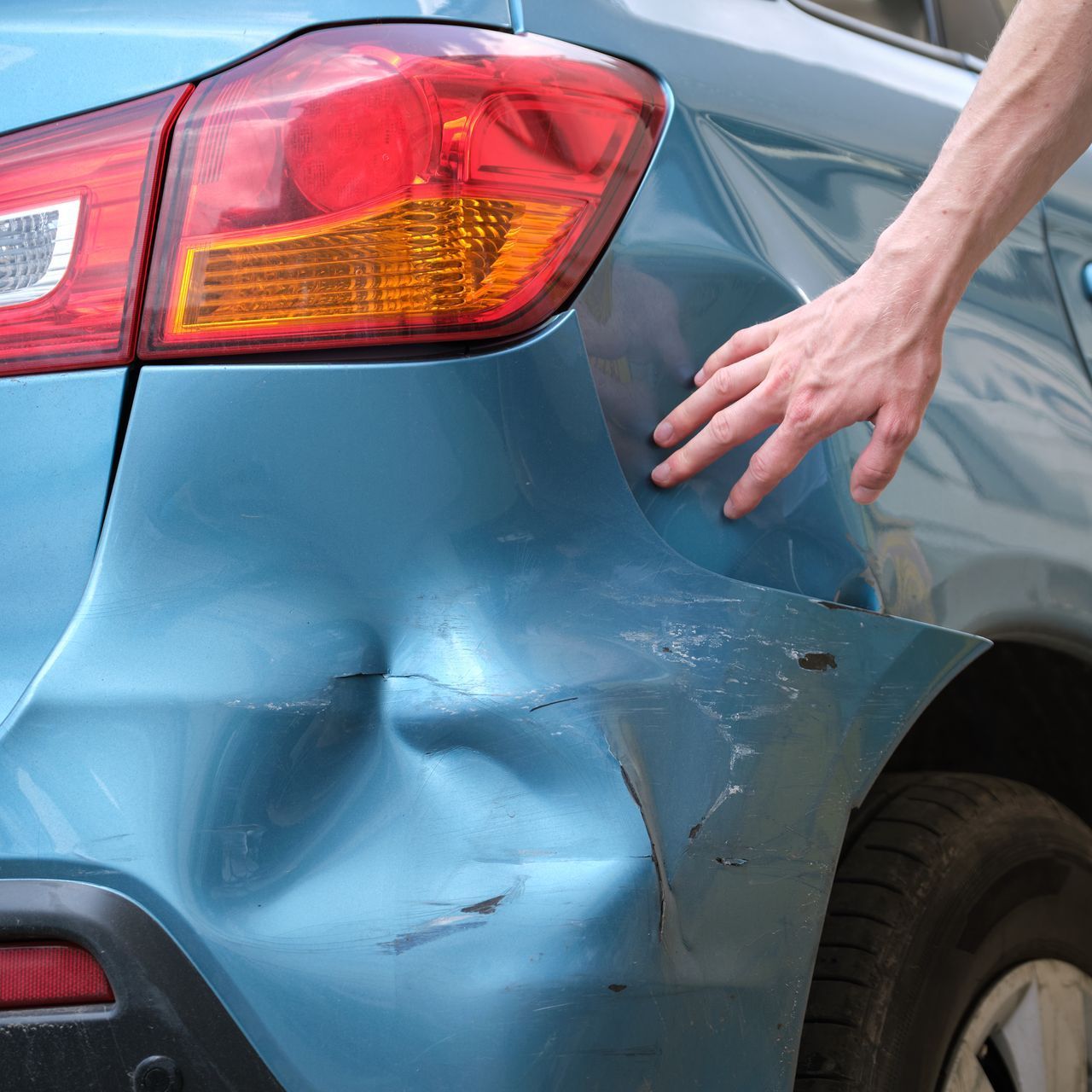 blue car with hand pointing to rear bumper damage