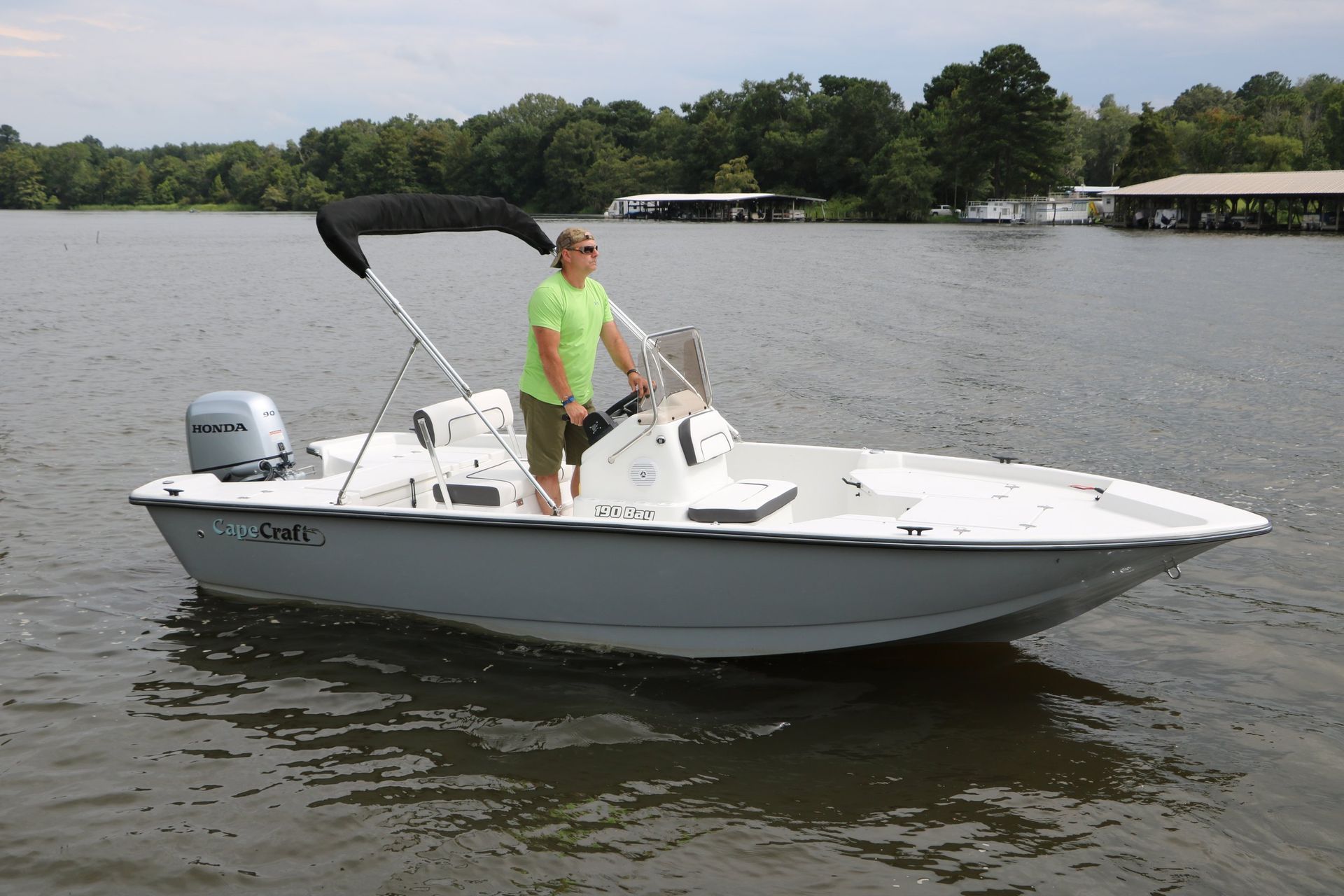 A man in a green shirt is standing on a boat in the water.