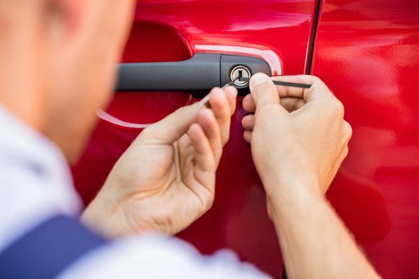 A man is using a screwdriver to open the door of a red car.