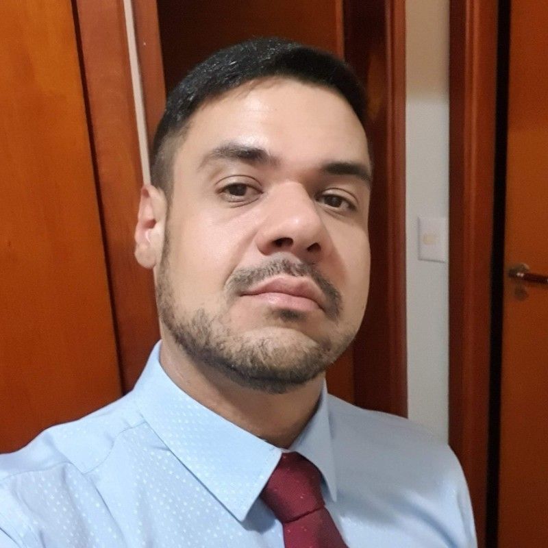 Um homem com barba está vestindo uma camisa azul e gravata vermelha.