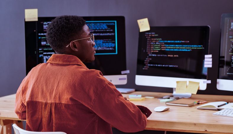 Data cleansing: na imagem, um homem sentado em frente a duas telas que mostram tela de códigos