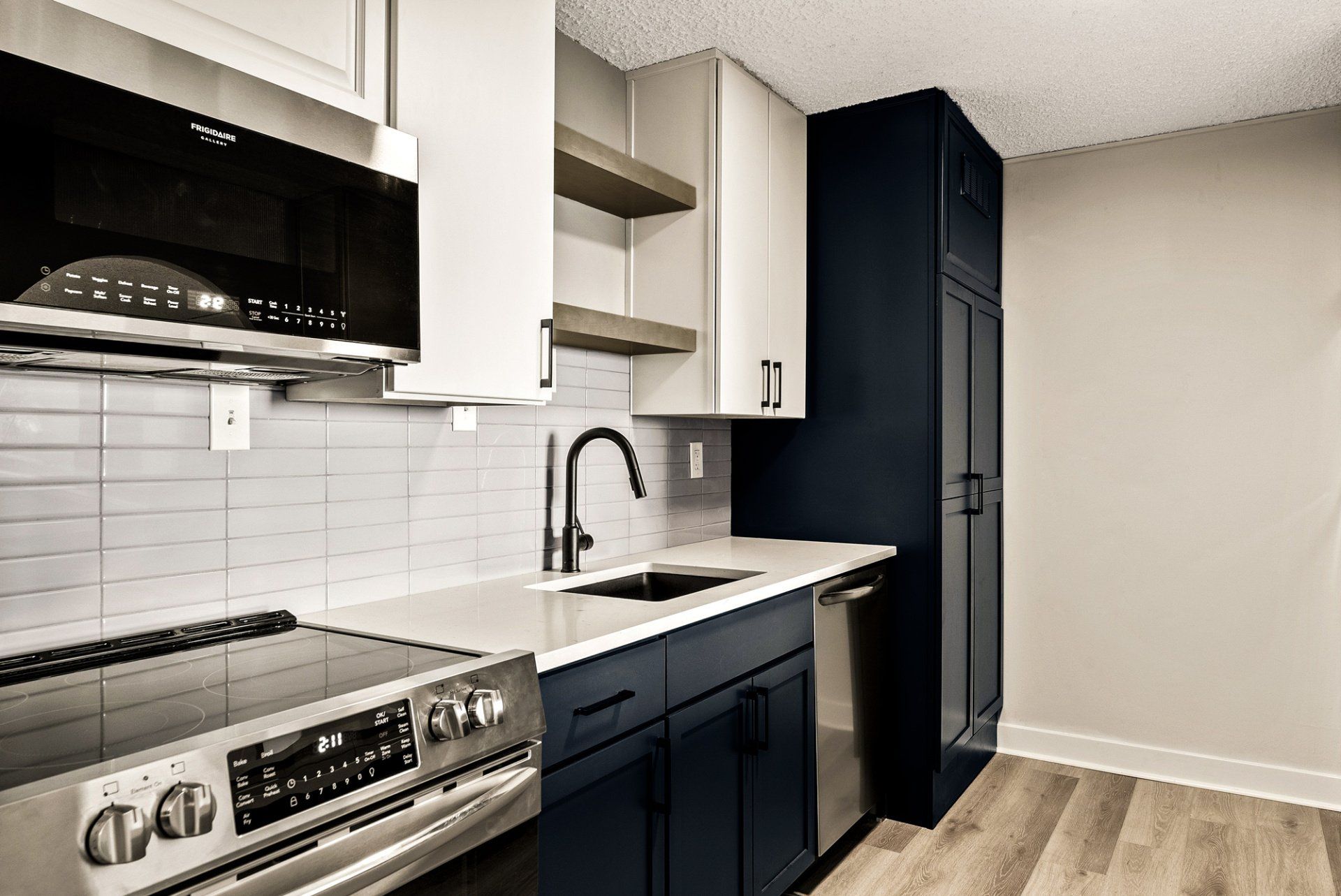 A kitchen with blue cabinets , a stove , a sink , and a microwave.