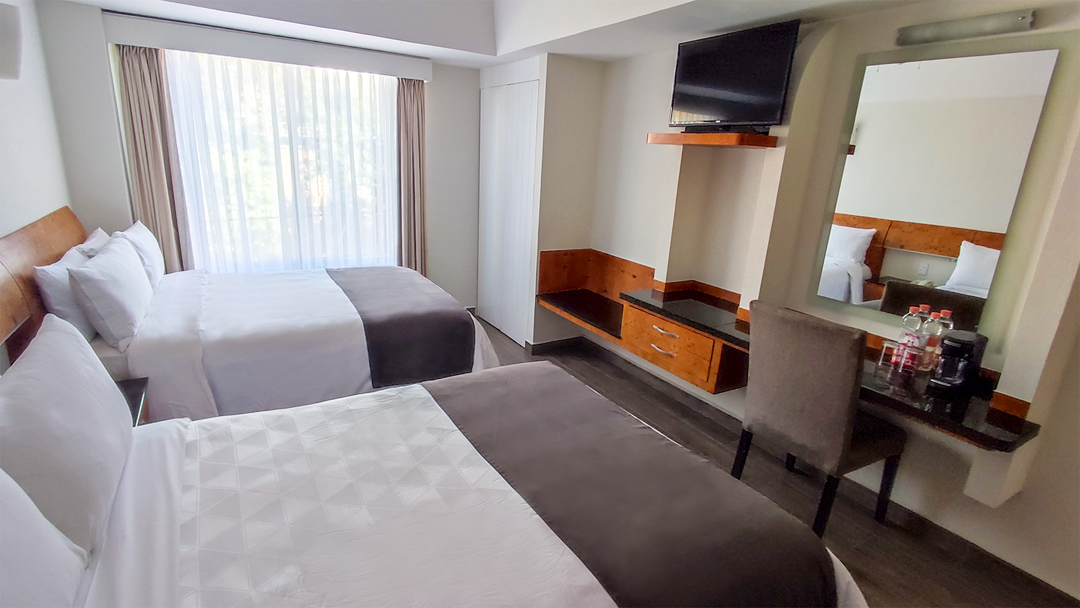 A hotel room with two beds , a desk , a television and a mirror.