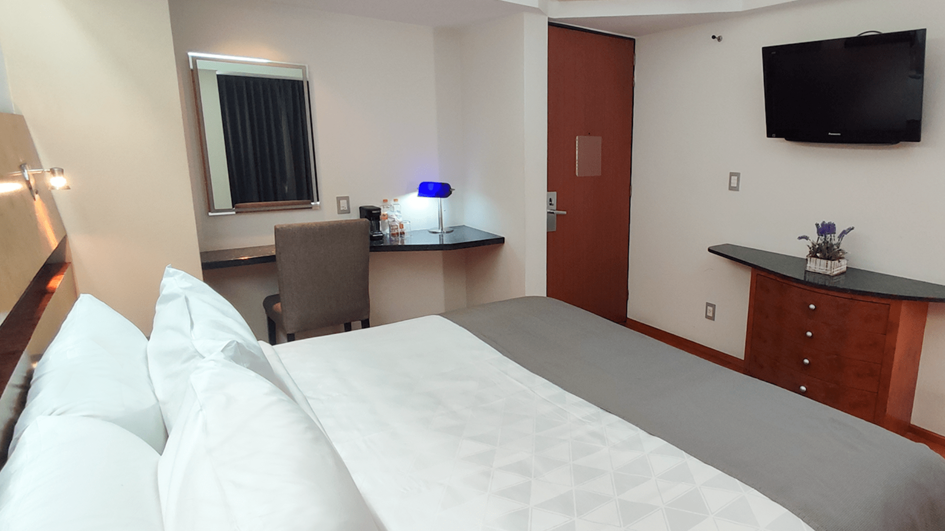 A hotel room with a bed , desk , chair and television.