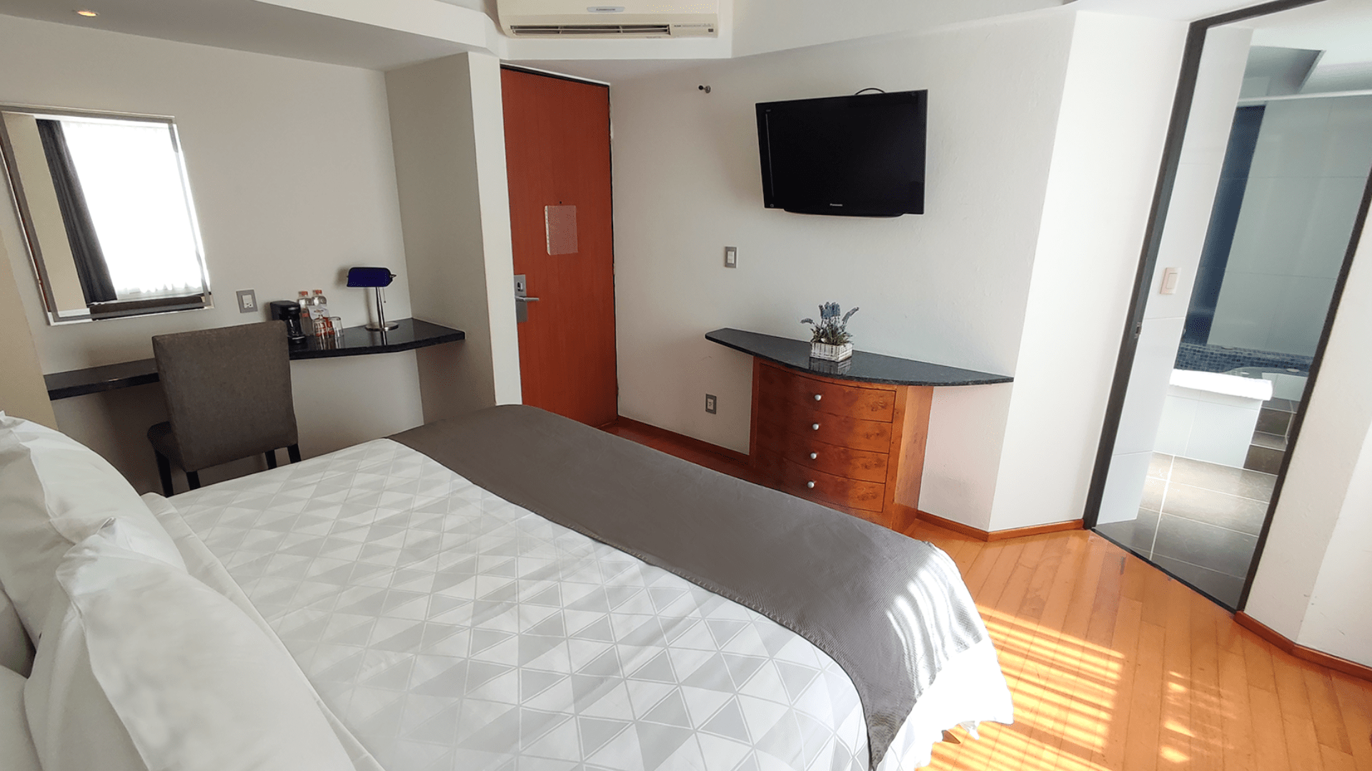 A hotel room with a bed , desk , television and mirror.