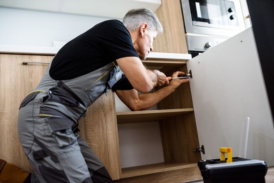 Person installing kitchen cabinets with a power drill in a modern kitchen