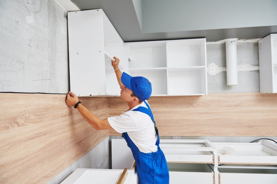 Worker in blue overalls installing a wood panel on a kitchen wall