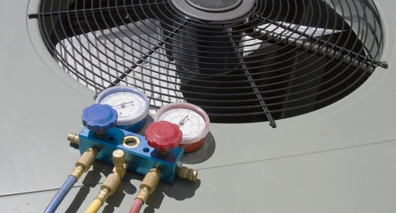 A manifold gauge set with blue and red dials rests on top of an outdoor air conditioning unit.