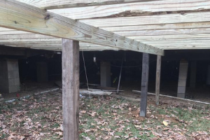 Wooden beams supported by vertical posts beneath a deck, with cinder block piers visible in the background.