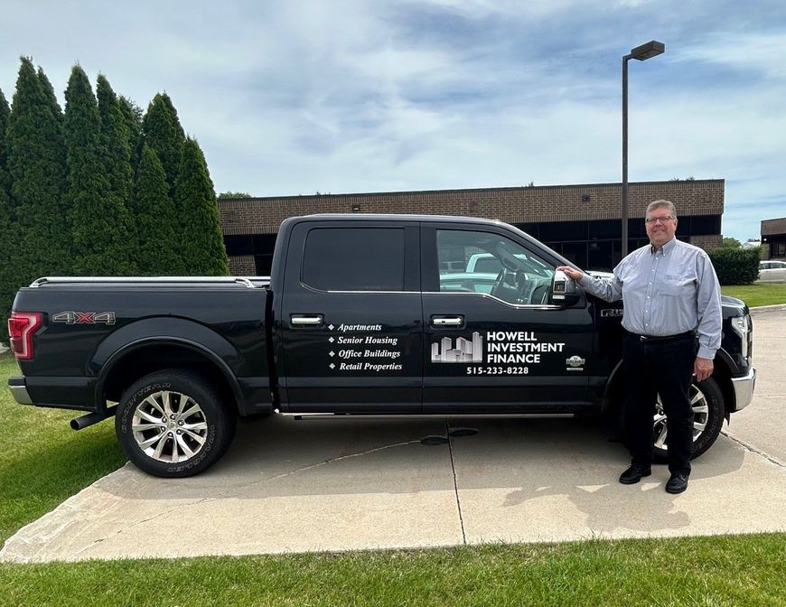 A man is standing next to a black pickup truck.— Ames, IA — Howell Investment Finance