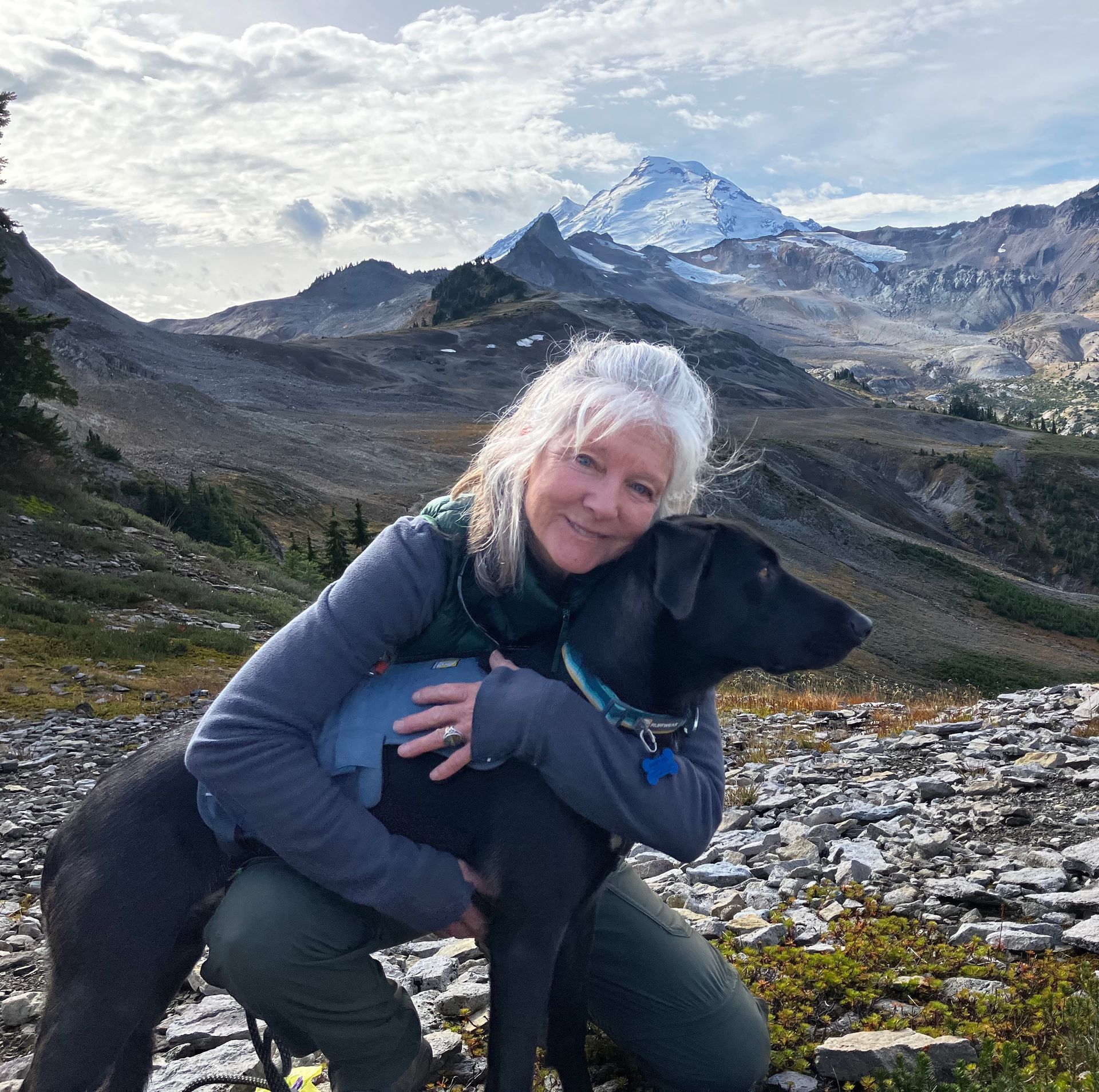A woman is hugging a black dog in front of mountains