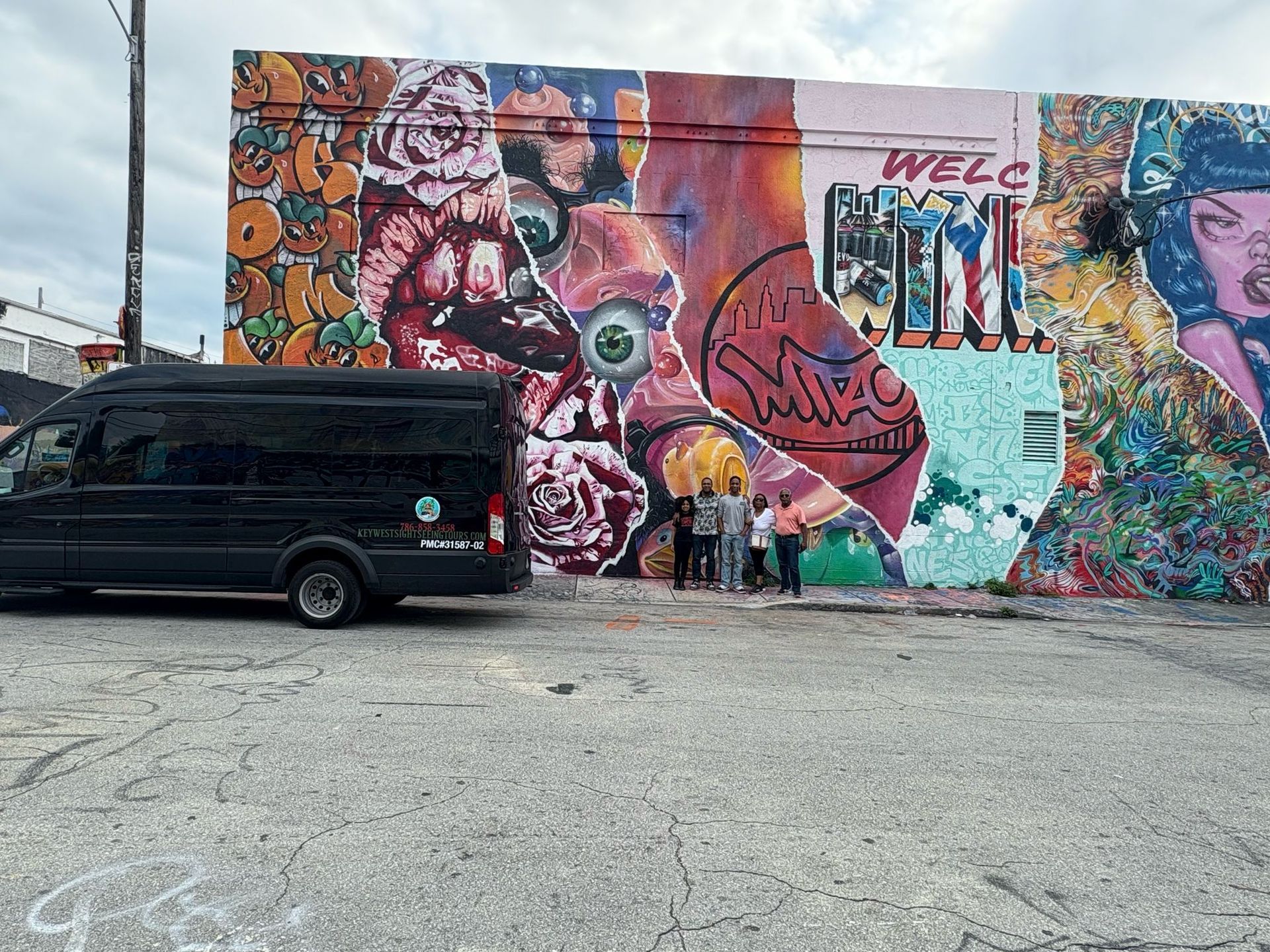 Tourists posing in front of the Miami tour bus at Wynwood Walls, excited to explore the vibrant street art scene.