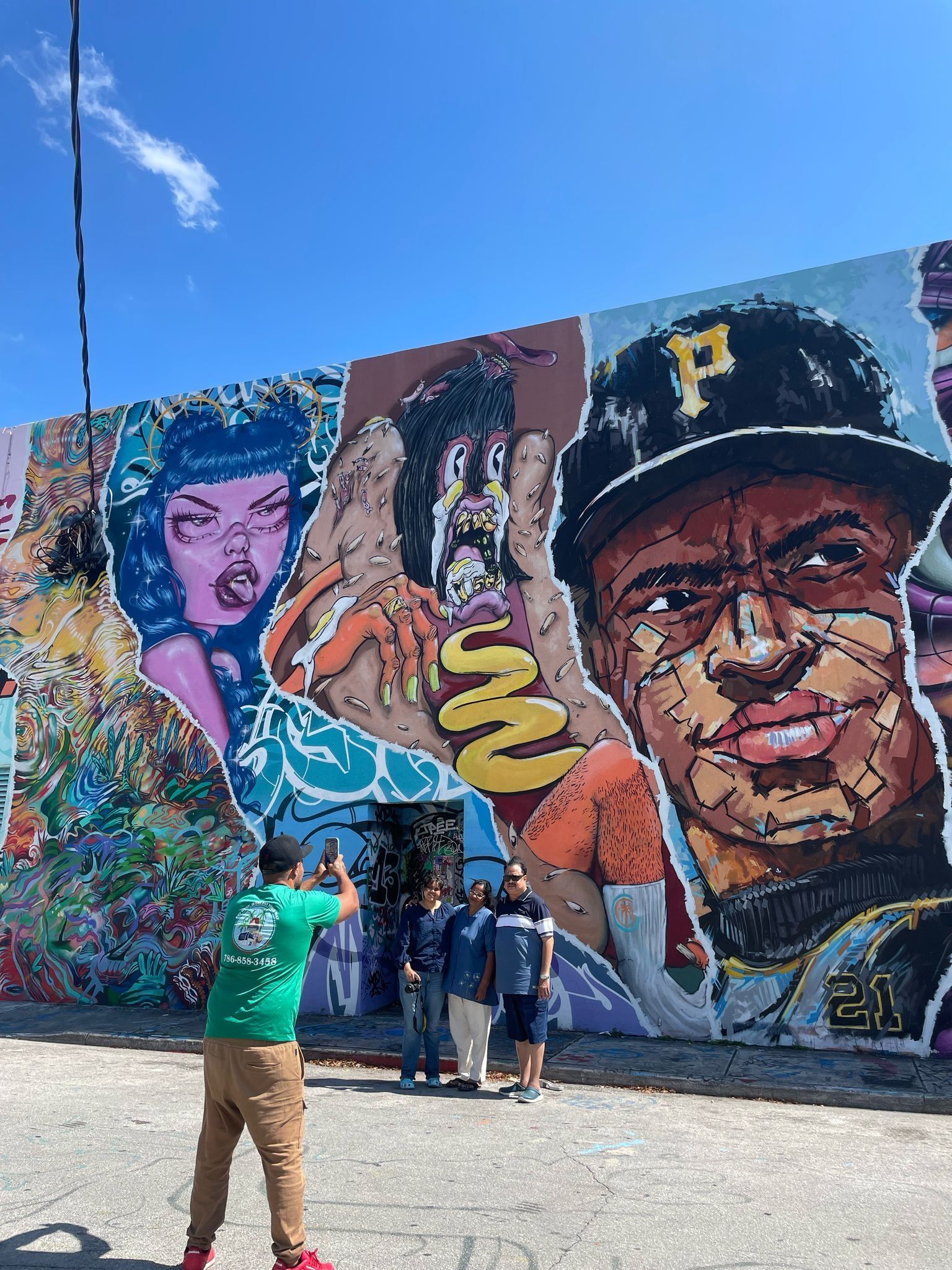Wynwood Walls Mural with tour guide with green uniform taking photos of them on the Miami City Tour by land