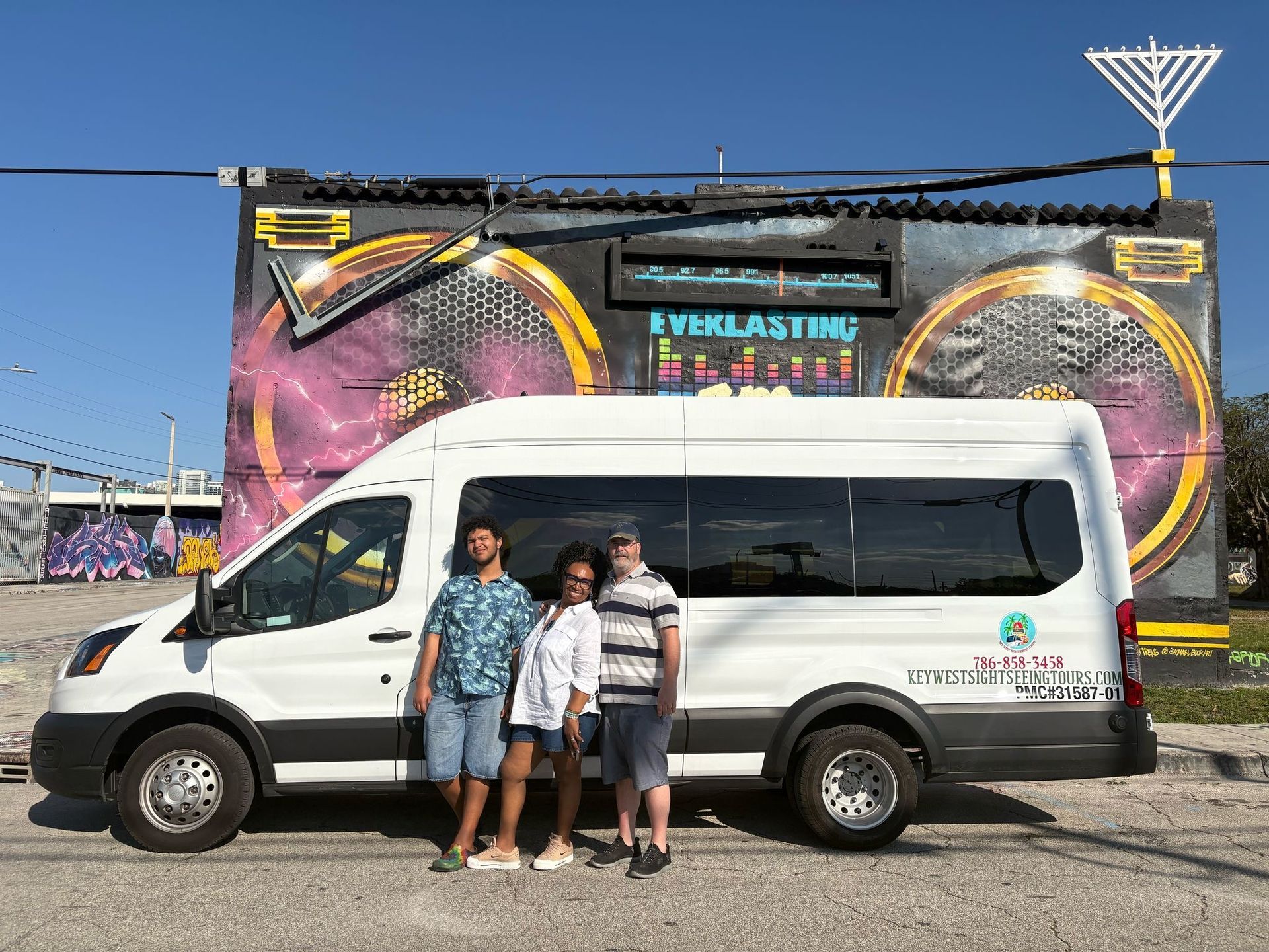 Tourists standing in front of the Miami tour bus at Wynwood Walls, taking photos and enjoying the vibrant street art murals in Miami's art district.