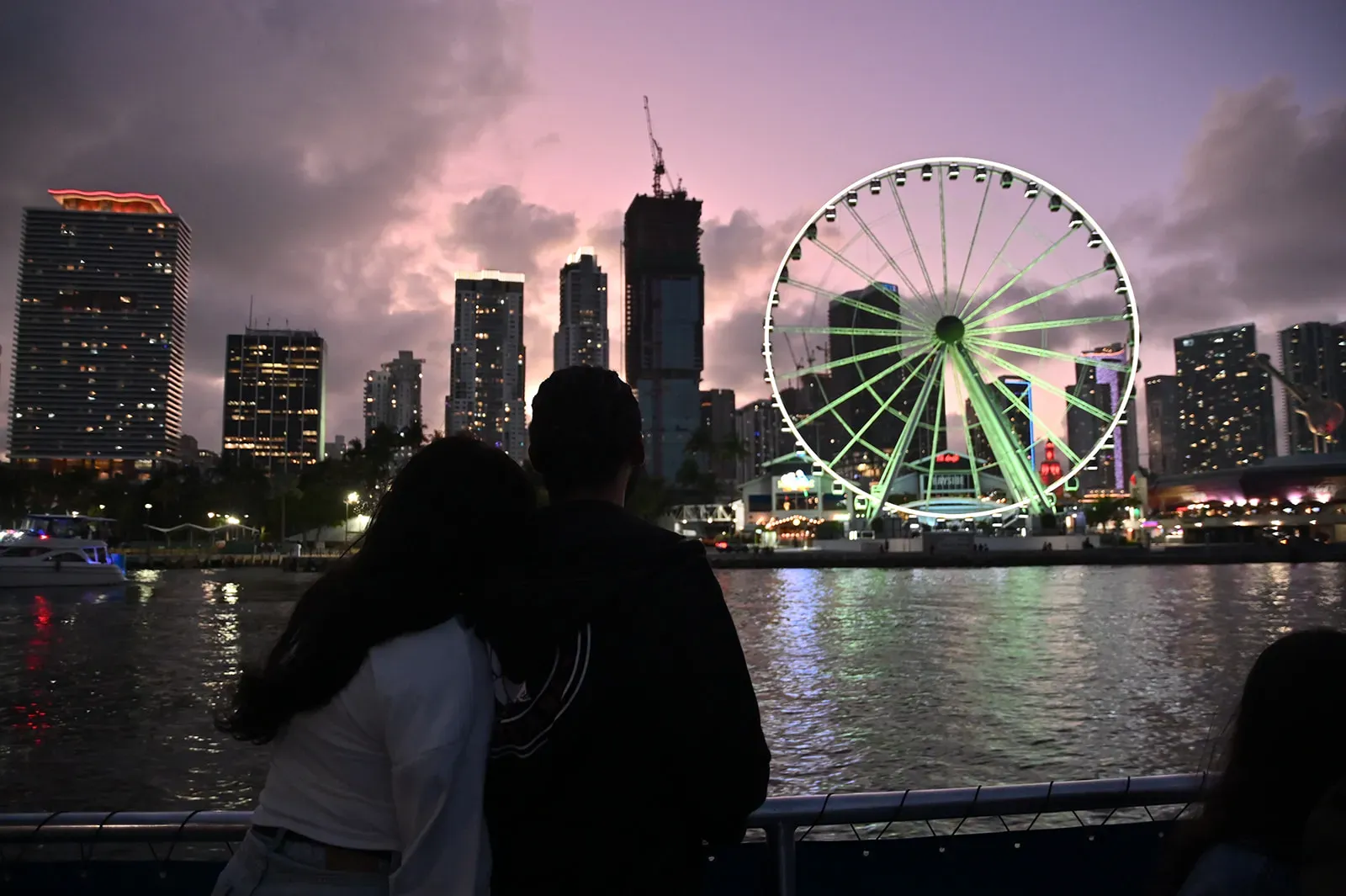 Couple admiring the Downtown Miami skyline at dusk from Biscayne Bay with the Skyviews Miami Observation Wheel in the foreground.