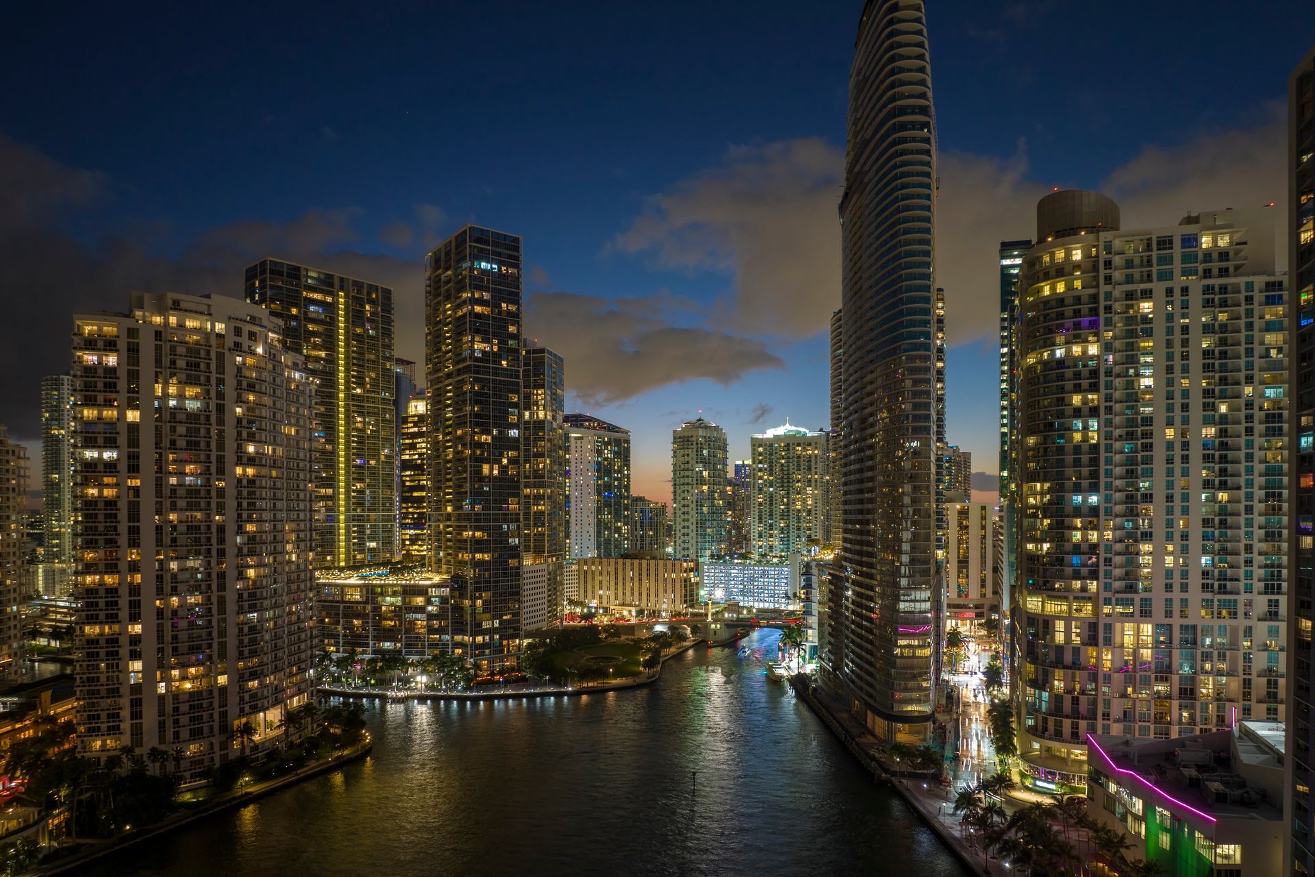 Night view of the Miami River with downtown and Brickell skyline illuminated and reflected on the water.