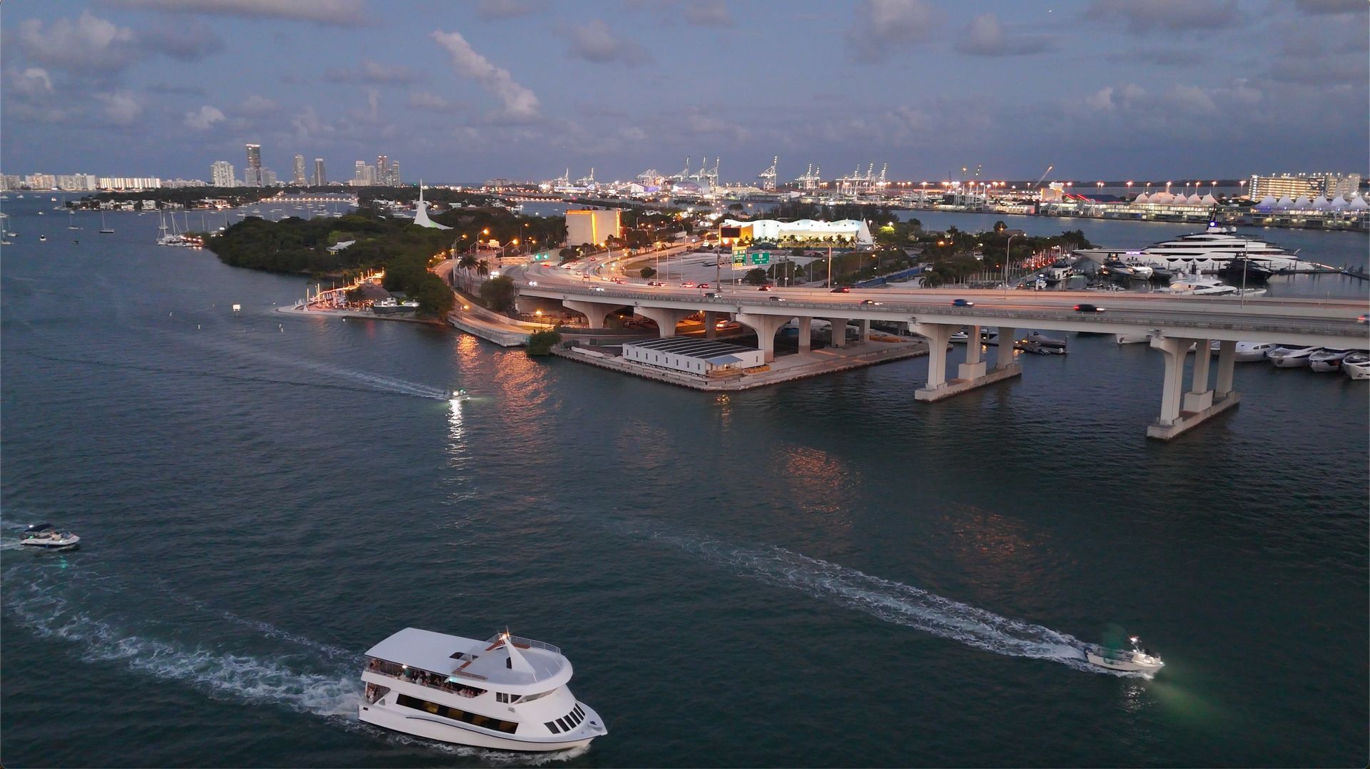 A Miami sightseeing sunset cruise boat sailing through Biscayne Bay with the city skyline and bridges glowing at dusk.