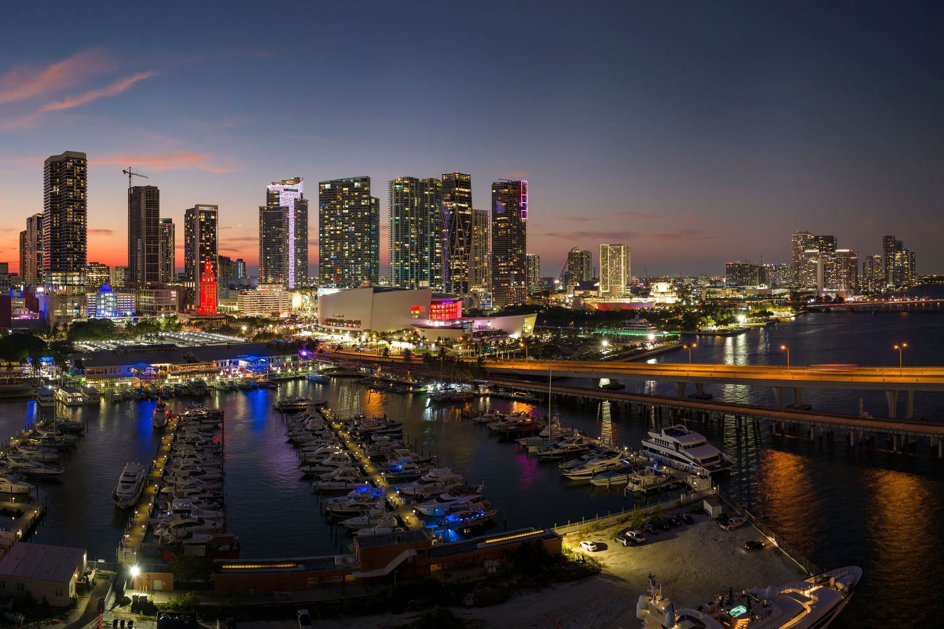 Miami skyline at dusk with downtown and Brickell buildings overlooking Biscayne Bay and marina lights.