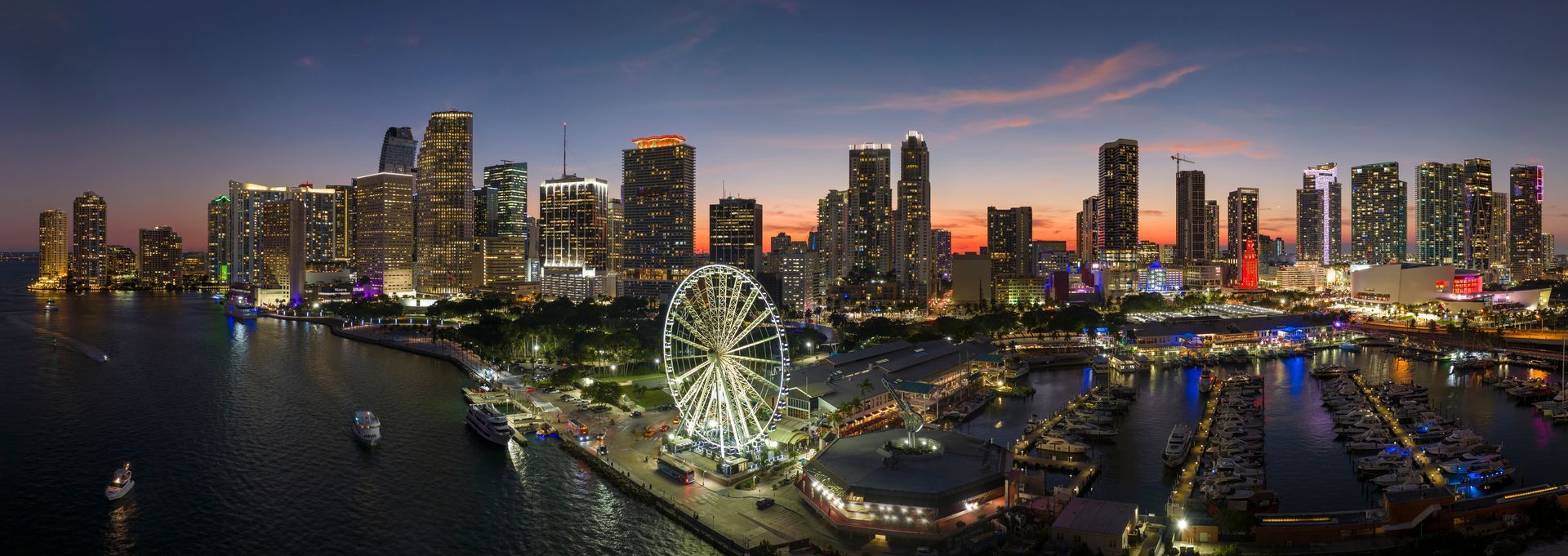 Miami skyline at night overlooking Biscayne Bay with Skyviews observation wheel and illuminated downtown buildings.