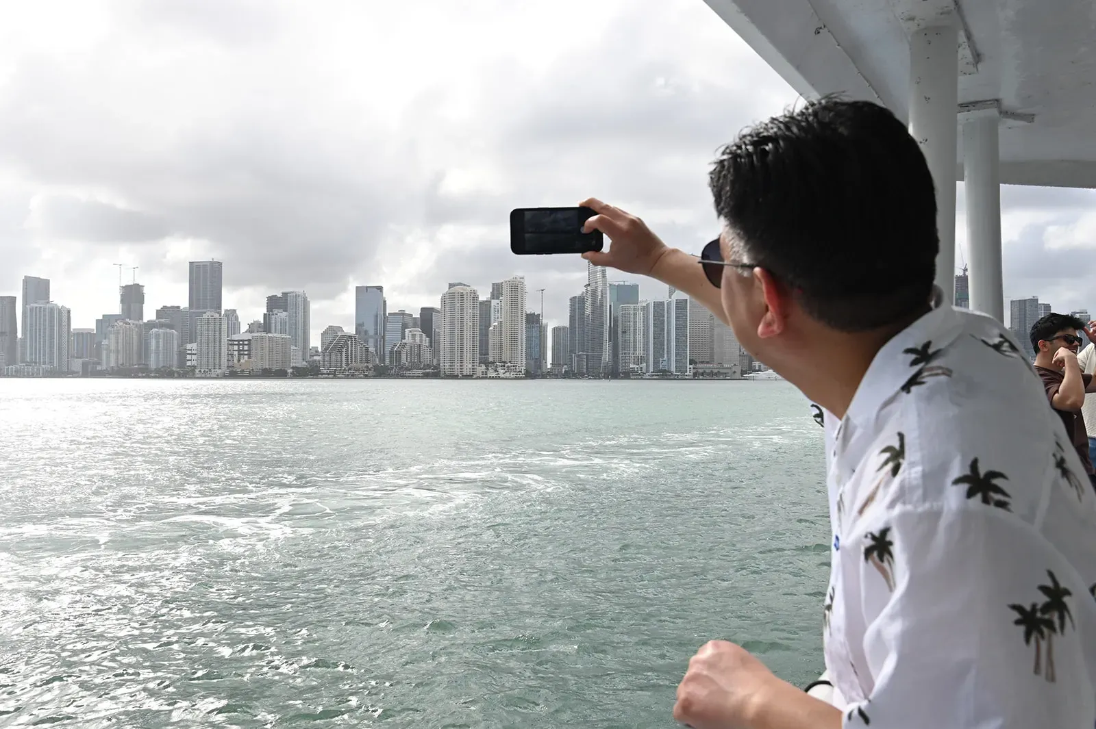 Person photographing the Miami skyline from Biscayne Bay during a sightseeing cruise with Downtown Miami in the background.