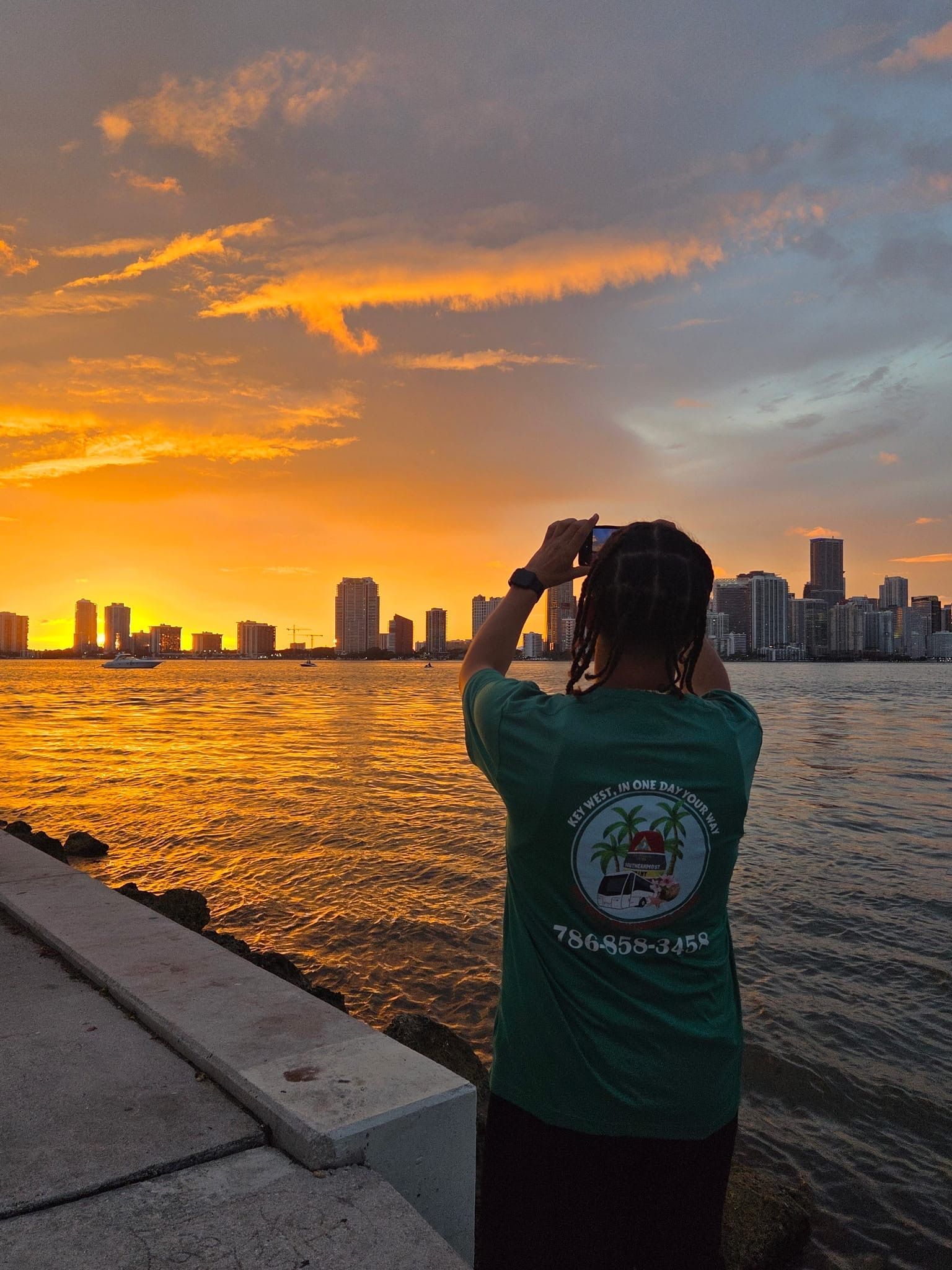 Person photographing the Miami skyline at sunset from land along Biscayne Bay