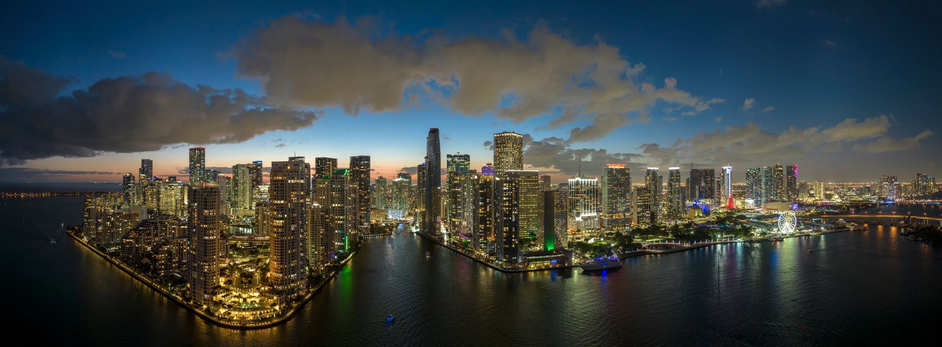 Panoramic night view of the Miami skyline with downtown and Brickell illuminated across Biscayne Bay.