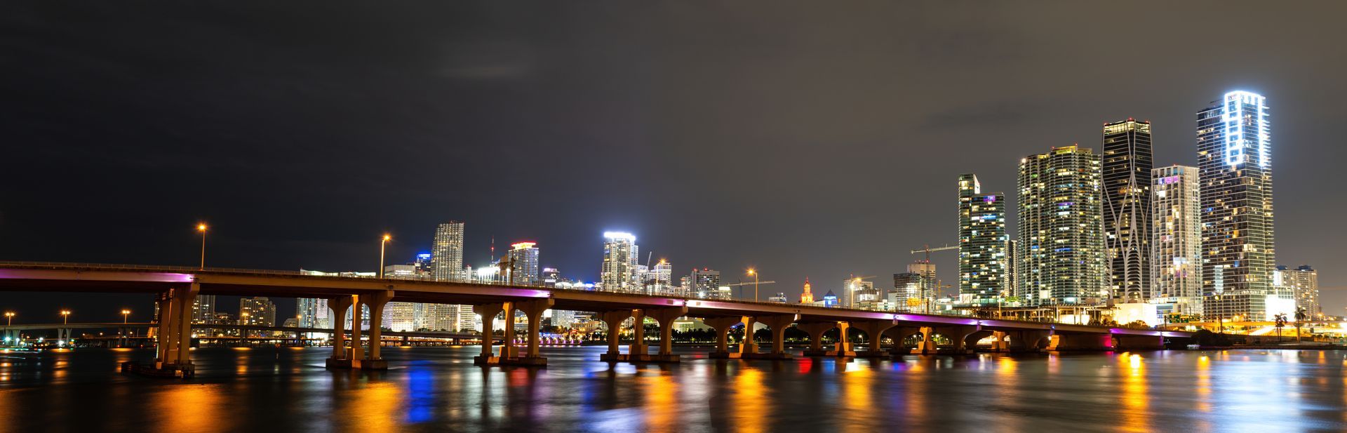 Miami night cruise views of the Port of Miami with downtown skyline illuminated across the water at night.