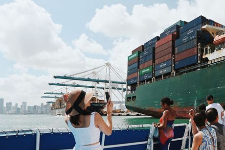 Passengers on a Miami boat cruise viewing massive container ships at the Port of Miami with the city skyline in the background