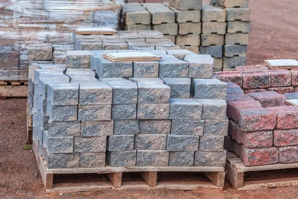 Pallets of Gray, Tan, and Red Bricks Stacked Outdoors on A Reddish Surface — Gladstone Garden & Landscaping Supplies In Burua, QLD