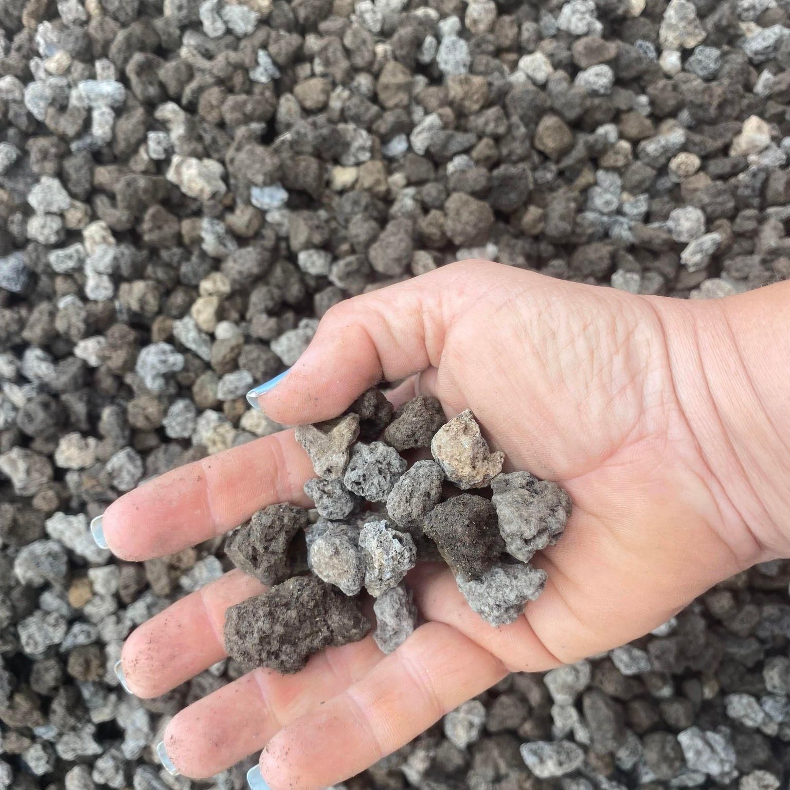 Hand Holding a Handful of Gray and Brown Lava Rocks — Gladstone Garden & Landscaping Supplies In Biloela, QLD