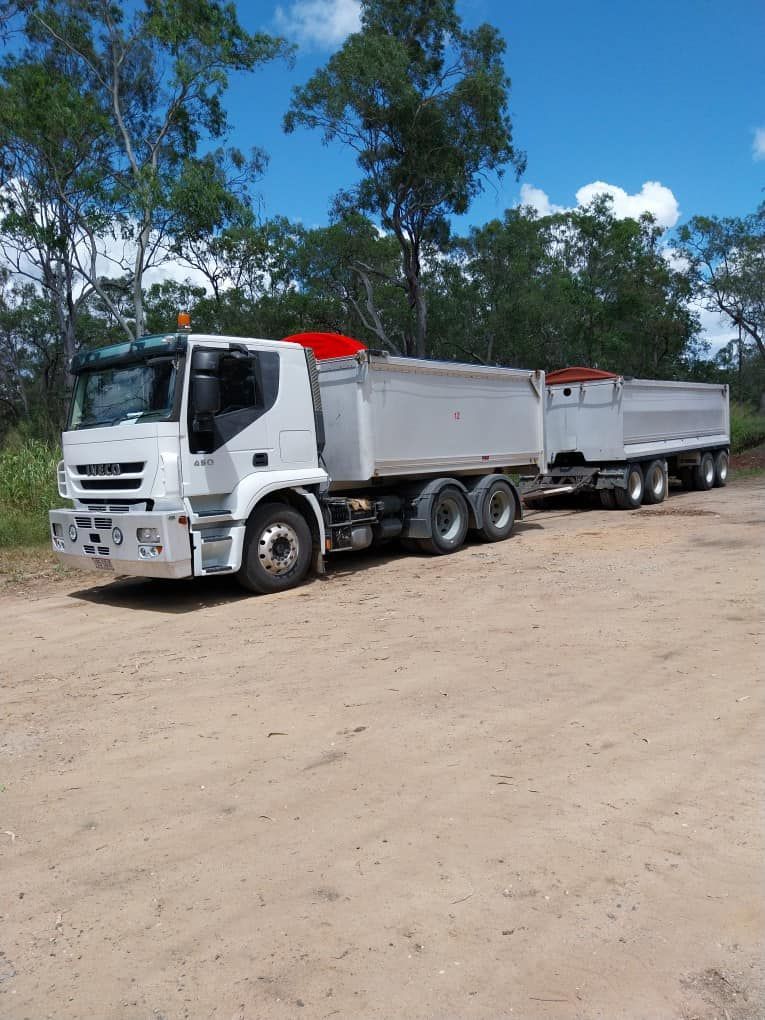 White Dump Truck with Two Trailers on A Dirt Road, Trees in The Background, Blue Sky — Gladstone Garden & Landscaping Supplies In Burua, QLD