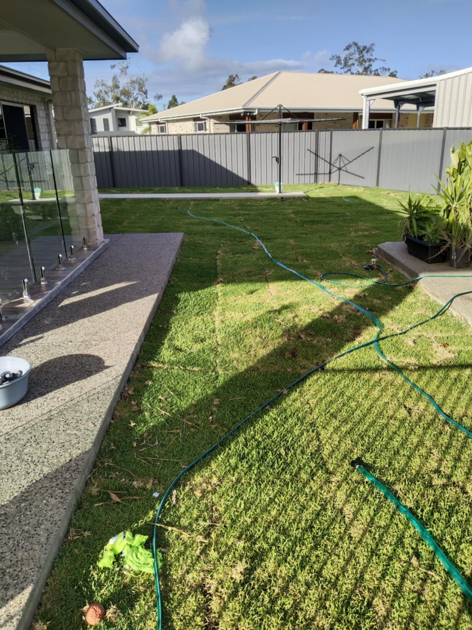 Green Lawn with A Hose, Adjacent to A Patio, and A Fence in The Background — Gladstone Garden & Landscaping Supplies In Burua, QLD