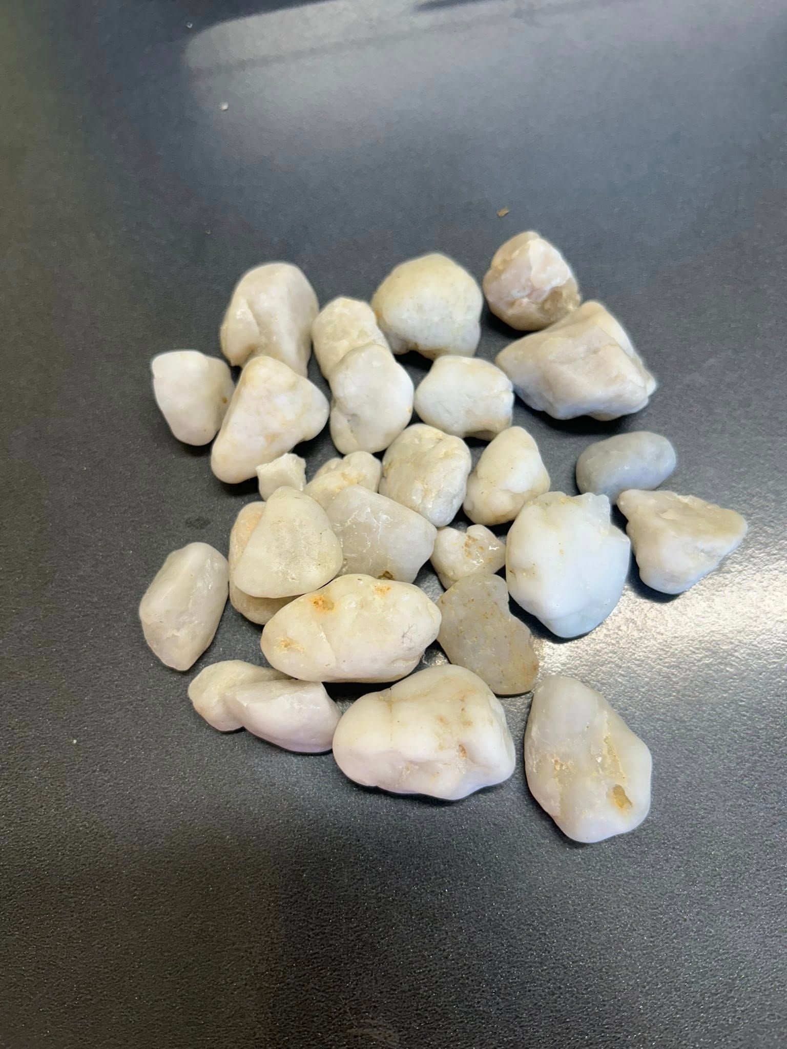 Pile of Smooth, Off-White River Rocks on A Dark Surface — Gladstone Garden & Landscaping Supplies In Burua, QLD