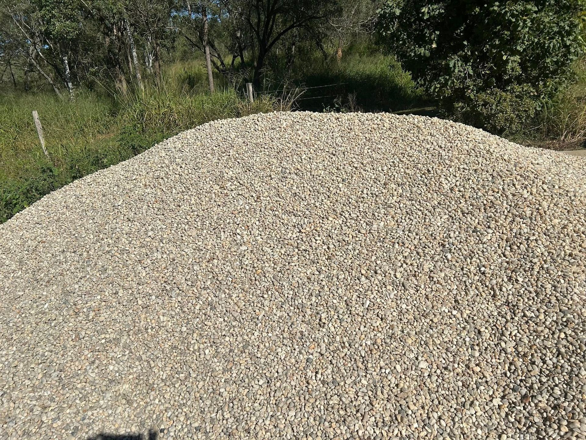 Pile of Light-Colored Gravel Against a Background of Green Trees and Vegetation — Gladstone Garden & Landscaping Supplies In Burua, QLD